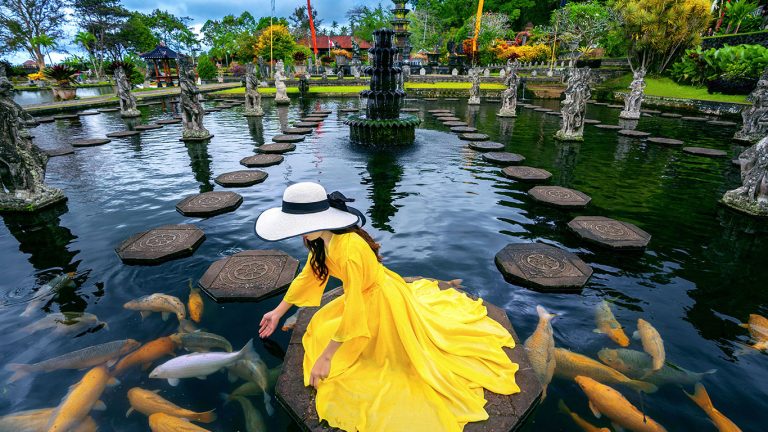 Woman feeding colorful fish in pond at Tirta Gangga Water Palace in Bali, Indonesia.