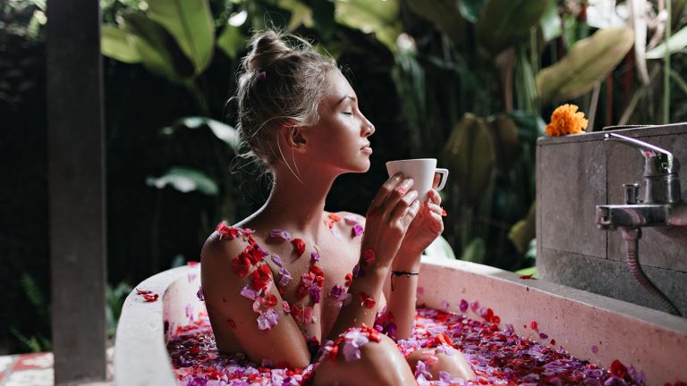Refined girl sitting in bath on nature background. Wonderful caucasian lady relaxing during spa and drinking tea.